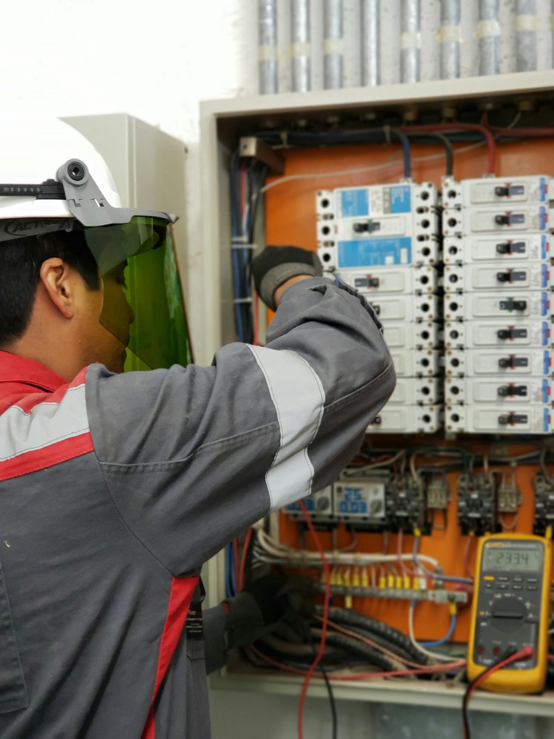 Teknisyen, devre kesiciler ve kablolarla açık bir elektrik panosunu inceliyor.